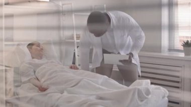 Destekleyici Afrikalı Amerikalı doktorun, ameliyattan sonra hastane koğuşunda yatan olgun kadın hastayı ziyaret etmesinin yavaşlığı.