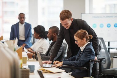 Modern ofiste iş arkadaşlarıyla çalışırken tekerlekli sandalye kullanan başarılı bir iş kadınının yüksek açılı portresi.