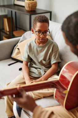 Evde müzik hocasıyla gitar çalmayı öğrenen Afrikalı Amerikalı bir çocuğun dikey portresi.