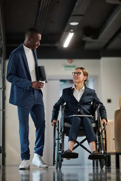 カメラに向かって移動しながら 現代のオフィスで同僚と話をしながら 車椅子を使用して成功した実業家の垂直長さの肖像画 — ストック写真