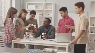 Kimya dersi sırasında moleküler modelleri incelerken Afrikalı Amerikalı öğretmenlerinin masasının etrafında duran orta sınıf öğrencilerinin orta yavaşlığı.