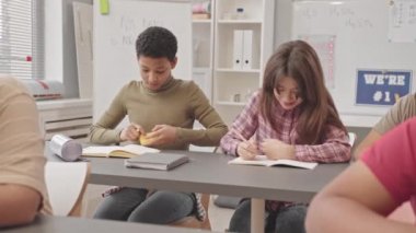 Modern sınıflarda öğretmenler sıralarda yürürken Afrikalı Amerikalı bir kızın fen sınavında kopya çekmeye çalışmasının orta derece yavaşlığı.