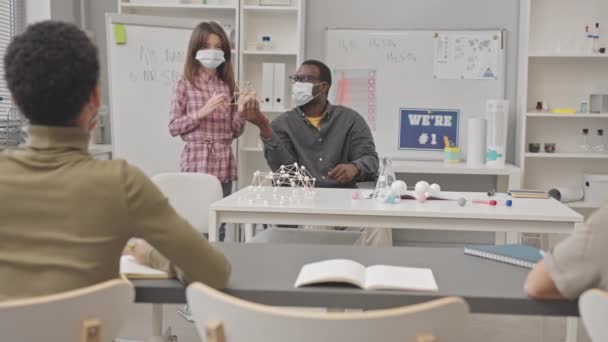 戴口罩的小学生慢吞吞地报告站在非裔美籍化学教师旁边拿着塑料分子模型的分子化合物 — 图库视频影像