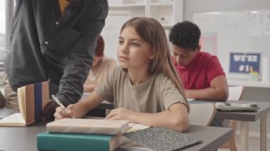 Tanımlanamayan Afro-Amerikan öğretmenlerin belini kaldırın. Bayan öğrenci yazma testinin masasında durup ona yardım edin.