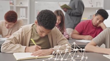 Farklı ortaokul öğrencilerinin belden yukarısına vurması ve modern sınıfta Fen dersi alan kızların defter defterlerine not alması.