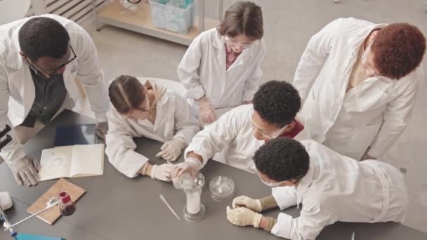研究室のコートを着たアフリカ系アメリカ人の先生や保護ガラスを身につけたアフリカ系アメリカ人の先生が 実験室の煙を液体で観察する授業で化学実験をしています — ストック動画