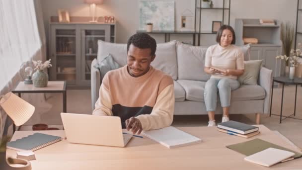 中等速度慢的已婚跨种族年轻夫妇在闭门造车期间呆在家里 在笔记本电脑上工作的非裔美国人 与他的支持他的妻子讨论项目 — 图库视频影像