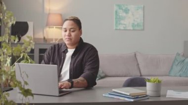 Orta yavaş, çift ırklı erkek kadın dizüstü bilgisayarla çalışıyor. Oturma odasında oturuyor. Beyaz kız arkadaşı ya da karısı kahvesini getiriyor.