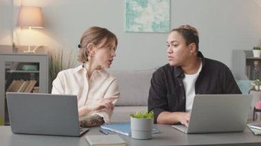 Oturma odasında yan yana oturan ve iş belgelerini tartışan iki ırklar arası lezbiyen çiftin beline dikkat edin.