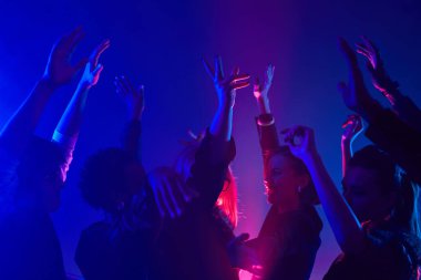 Kulüpte dans eden, neon ışıklarla aydınlatılan az sayıdaki kalabalık görüntüsü.