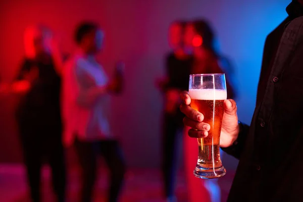 ネオンライトでパーティーでビールグラスを持っている認識できない若い男のクローズアップ コピースペース — ストック写真