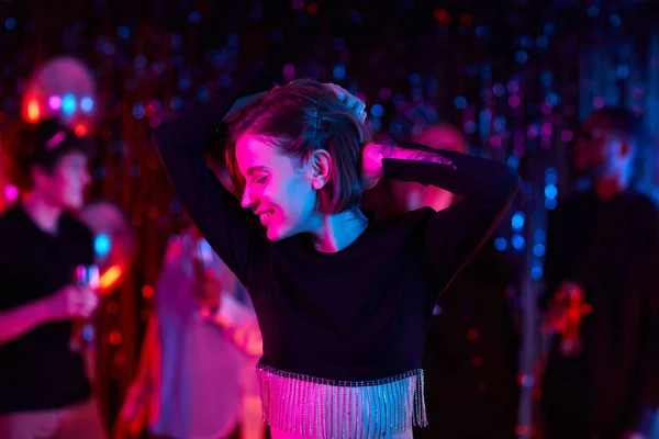Waist up portrait of carefree young woman dancing at party in neon lights, copy space