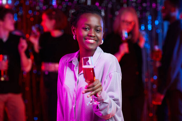 Waist up portrait of smiling African American woman holding drink at party in neon lights, copy space