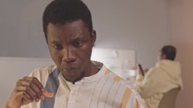 Akşamları kadın meslektaşımla ofiste otururken sağlıklı yiyecekler yiyen düşünceli genç siyahi adamın göğsünü kabart ve teslim tarihine yetiş.