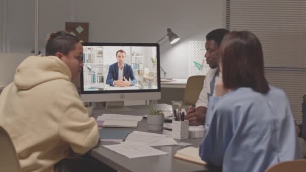 コンピュータを介して上司とオンラインビデオ会議を持っている多民族の同僚のスローモ 夜に近代的なオフィスに座って 会議の期限 — ストック動画