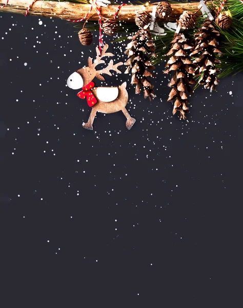 Weihnachtsdekor aus Tannenzapfen und hölzernen Hirschen auf dunklem Hintergrund. Weihnachtsgrußkarte mit Platz für Ihren Text. — Stockfoto