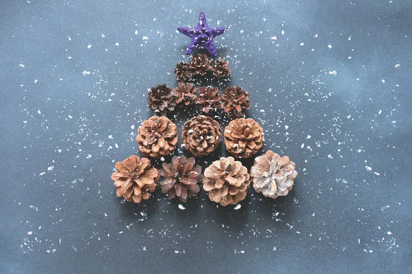 Christmas tree made of pine cones on dark blue background with sparkles. New year Color Trends, Attention-grabbing Palettes 2023 year. DIY jewelry. Close-up