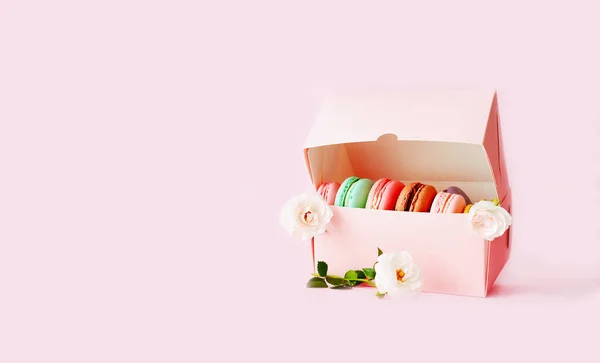 Gift box with colored macaroons on pink background with white roses. Bold hues for seasonal projects and basis designs. Close-up