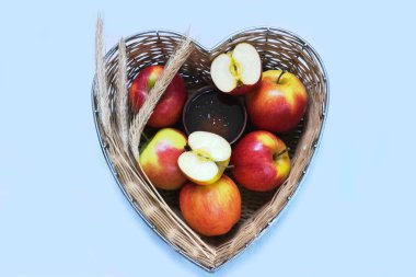 Red apples and ears of wheat in straw basket made in the shape of heart on blue background. Religious holidays concept - Jewish New Year or Transfiguration of the Lord. Copy space