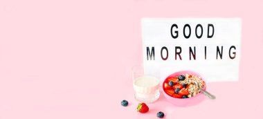 Oatmeal mit natural ingredients in pink bowl. Porridge with strawberries, blueberries and walnuts for healthy breakfast. Good morning word in light box. Creative copy space for seasonal projects, close-up