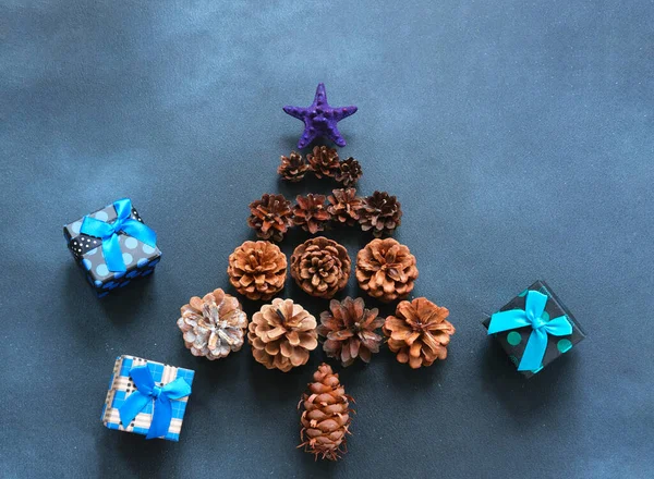 Christmas tree made of pine cones and gift boxes on dark blue background with sparkles. New year Color Trends, Attention-grabbing Palettes 2023 year. DIY jewelry.