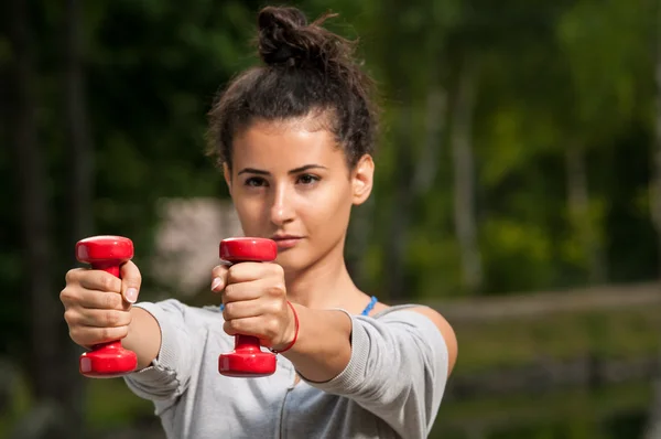 Woman exercising in the park with two red weights — Stock Photo, Image