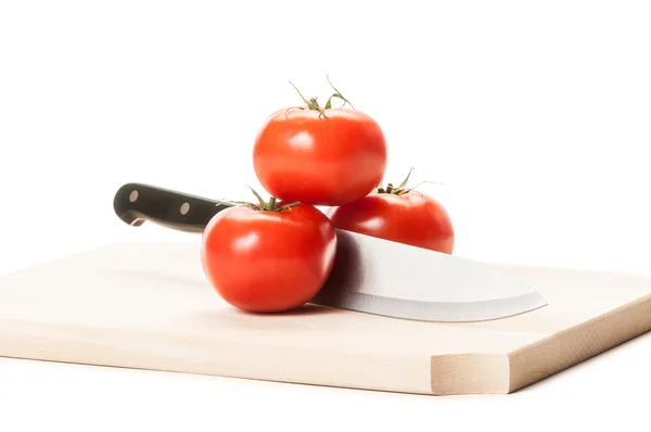 Knife between three tomatoes on wooden boar — Stock Photo, Image