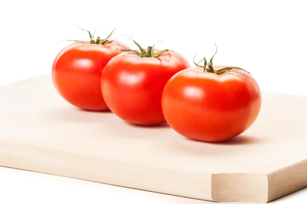 Três tomates em pé na linha em javali de madeira — Fotografia de Stock