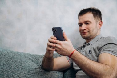 Gri tişörtlü yakışıklı blogcu elinde iPhone 12 Pro ile abonelerle iletişim kuruyor.