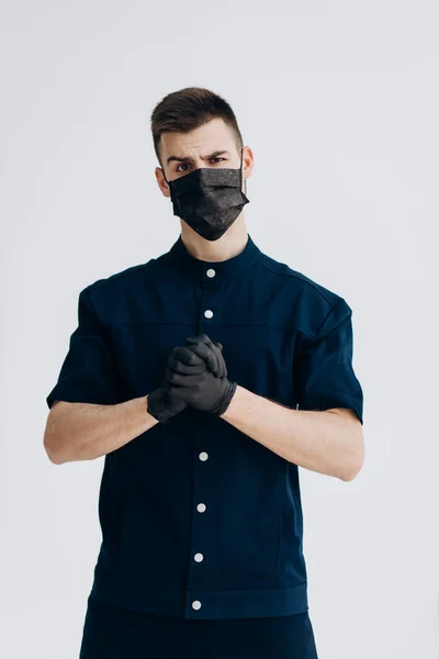 Male doctor in black gloves puts on mask against covid