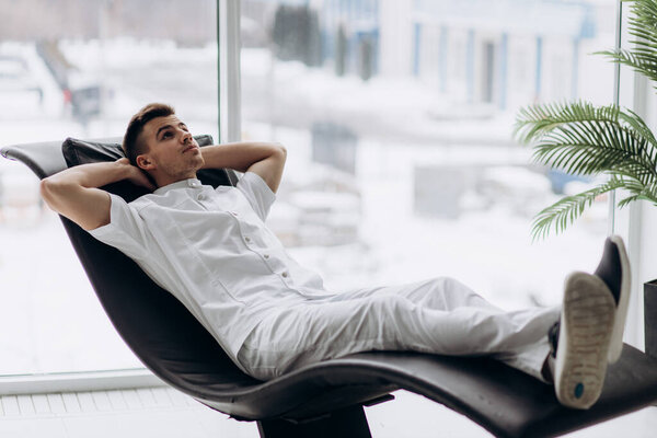 Young male dentists in white coats lies and smiles in a hospital chair