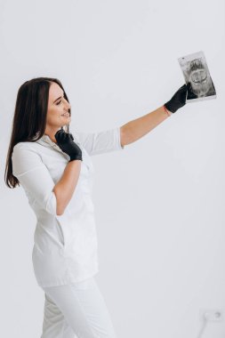 Beyaz önlüklü diş hekimi elinde dişlerinin röntgenini tutuyor.