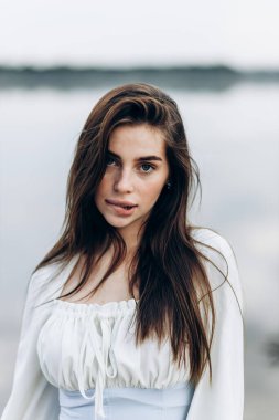 Beyaz elbiseli, mayolu, bronzlaşmış seksi vücutlu güzel sarışın genç kızın yaz hayat tarzı portresi tropikal ada sahilinde berrak suyla duruyor.