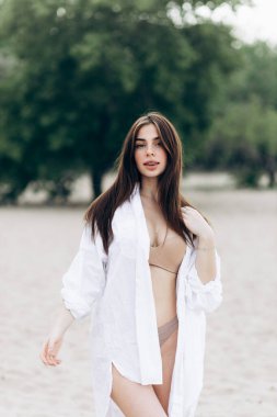 Beyaz tişört ve mayo giymiş bronzlaşmış seksi vücutlu güzel sarışın kızın yaz hayat tarzı portresi tropikal ada sahilinde berrak suyla duruyor.