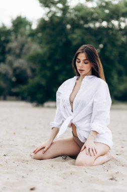 Beyaz tişört ve mayo giymiş bronzlaşmış seksi vücutlu güzel sarışın kızın yaz hayat tarzı portresi tropikal ada sahilinde berrak suyla duruyor.