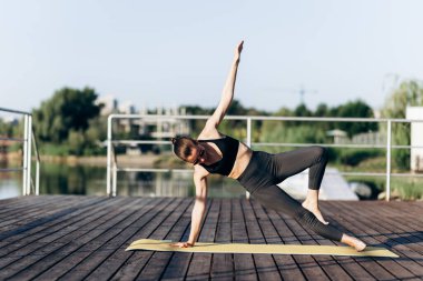 Spor kıyafetleri içinde bronzlaşmış seksi vücudu olan, yoga minderinde egzersiz yapan güzel, sarışın, mutlu bir genç kızın yaz portresi.