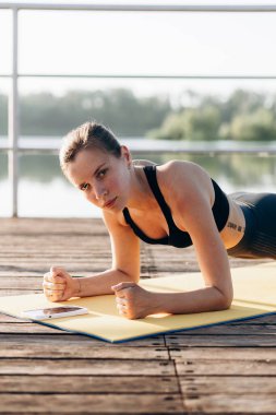 Spor kıyafetleri içinde bronzlaşmış seksi vücudu olan, yoga minderinde egzersiz yapan güzel, sarışın, mutlu bir genç kızın yaz portresi.