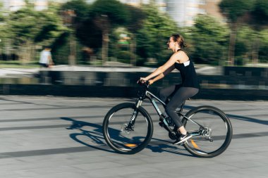 Spor kıyafetleri ve güneş gözlükleriyle bronzlaşmış seksi vücudu olan ve bisiklet süren güzel bir sarışının hayat tarzı portresi.