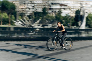 Spor kıyafetleri ve güneş gözlükleriyle bronzlaşmış seksi vücudu olan ve bisiklet süren güzel bir sarışının hayat tarzı portresi.