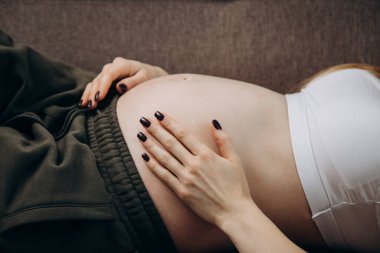 Yeşil pantolonlu hamile kız karnını okşuyor.