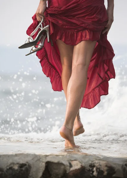 Sexy woman in red dress, steps on wet rock, next to sea — Stock Image Sexy woman in red dress, steps on wet rock, next to sea Stock Image