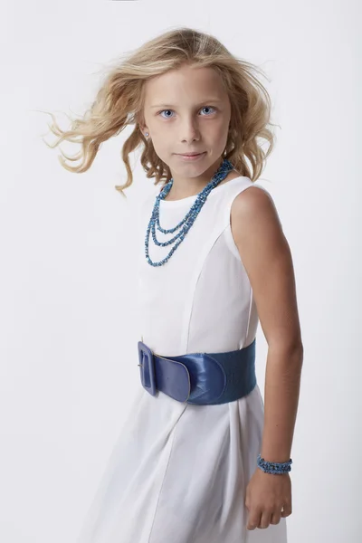 Petite fille blonde bouclée en robe blanche, accessoires bleus, fond blanc — Photo