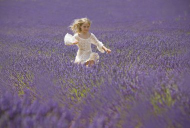 Happy little girl jumps in field of lavender clipart