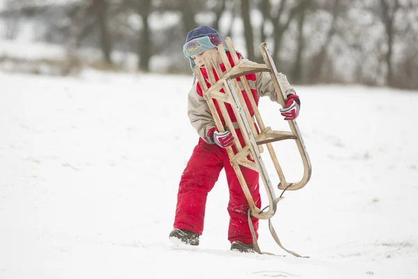 Niño en rojo, lleva su trineo en el campo de invierno —  Fotos de Stock