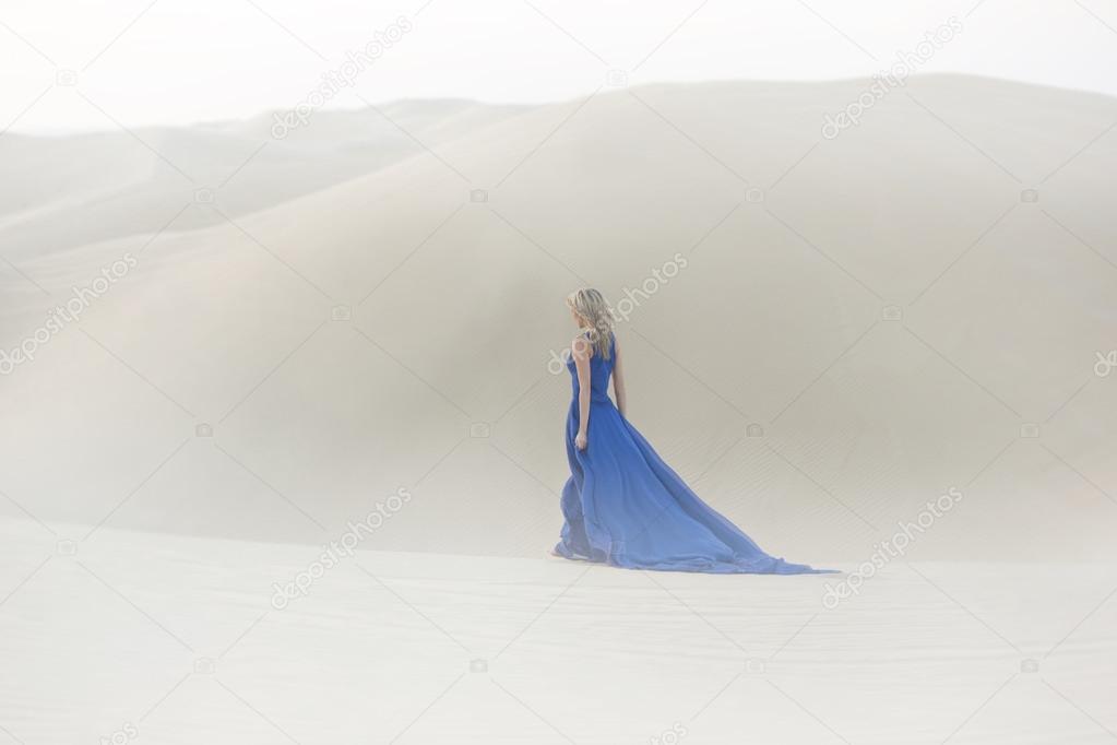 Beautiful young woman walks in desert, long, blue dress