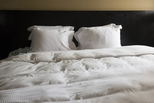 Двуспальная кровать в номере с белым одеялом и подушками — стоковое фото
