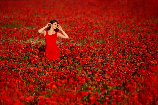 在一片红红的罂粟地里 纤细的黑发女人穿着红衣服摆姿势 — 图库照片