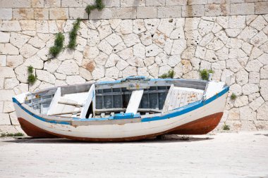 Güney İtalya, Otranto 'da bir duvarın yanında işe yaramaz eski bir balıkçı teknesi enkazı yatıyor..