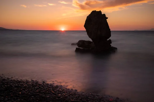 水平線に太陽を置き ギリシャのロードス島の背景に海の真ん中に興味深い形の岩が立っています ストック画像