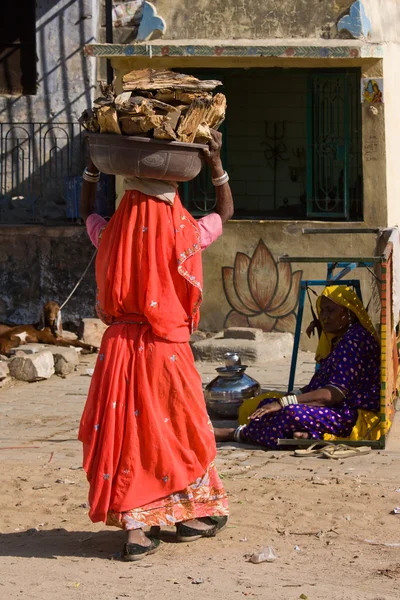 PUSHKAR, INDIA - 18 DE NOVIEMBRE: Una mujer no identificada con leña en la cabeza asiste al Camello Mela de Pushkar el 18 de noviembre de 2012 en Pushkar, Rajastán, India. Esta feria es el mayor comercio de camellos — Foto de Stock